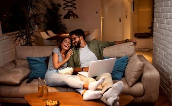 A couple relaxes on a couch with their feet up and laugh