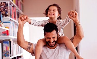 A man is holding a little girl on his shoulders in a living room.