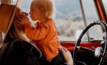 A woman kisses her child in the front seat of a truck.